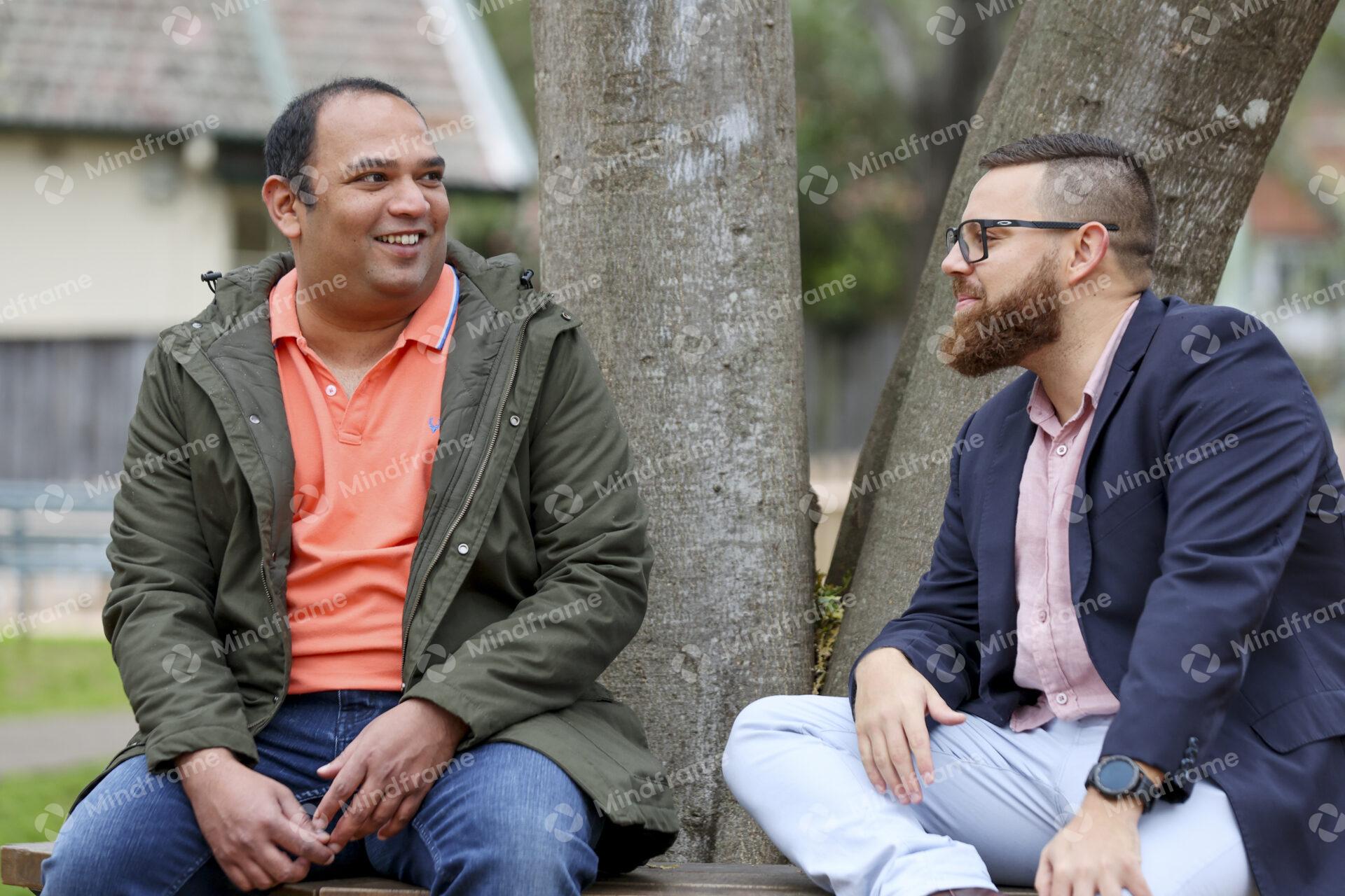 Two people talking and sitting outside in front of tree