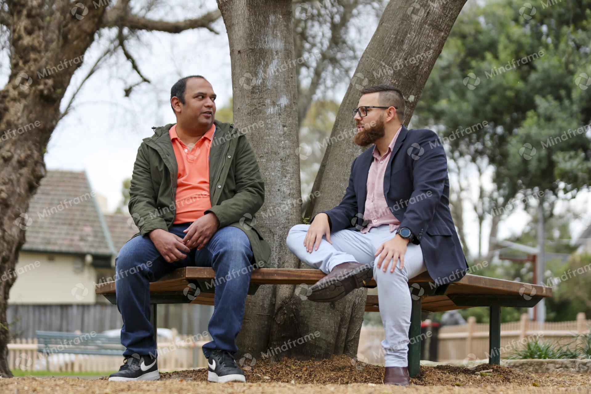 Two people talking and sitting on bench in front of tree