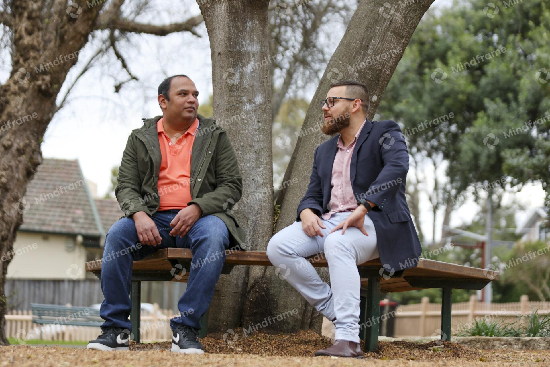 Two people talking and sitting on bench in front of tree