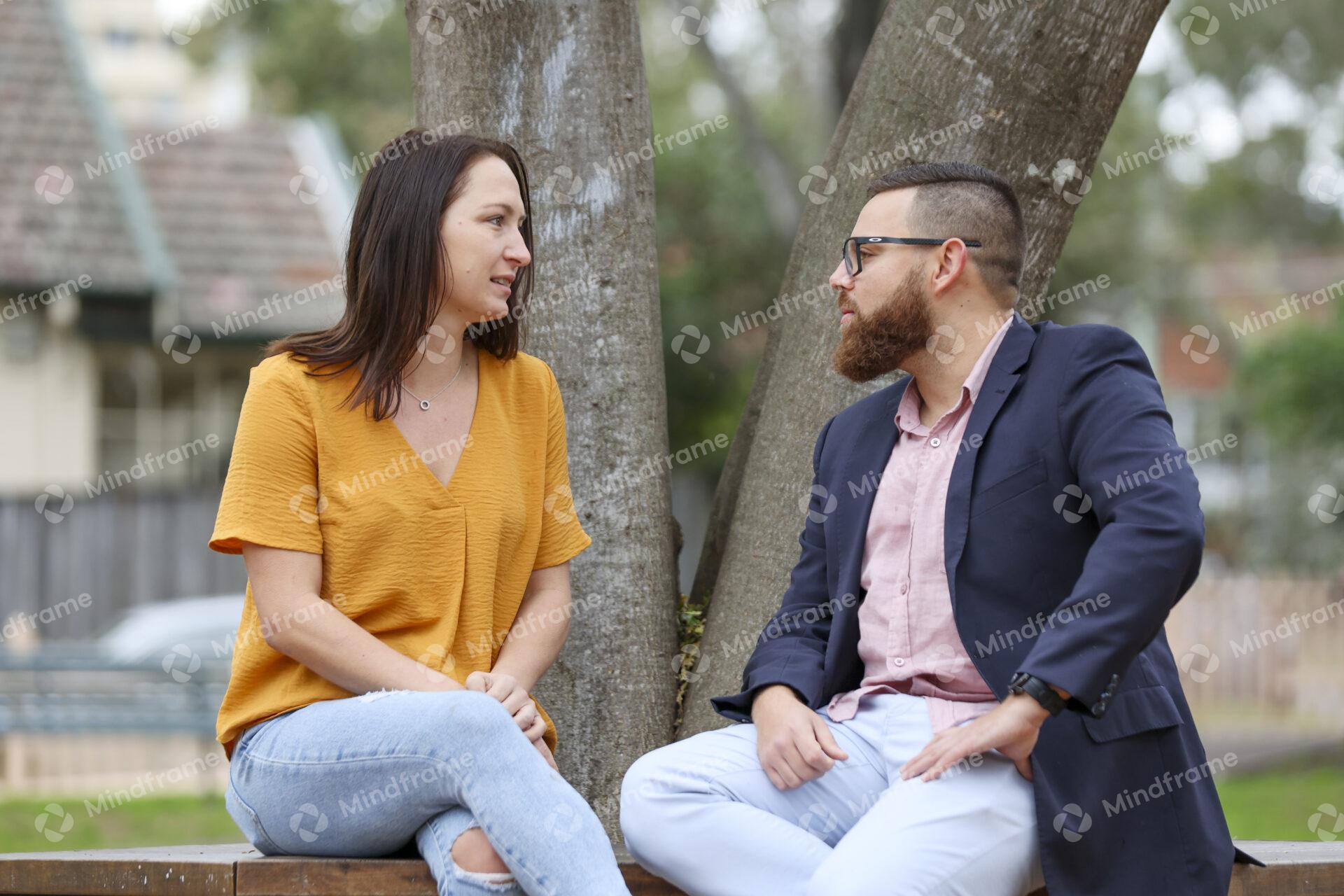 Two people talking and sitting on bench in front of tree