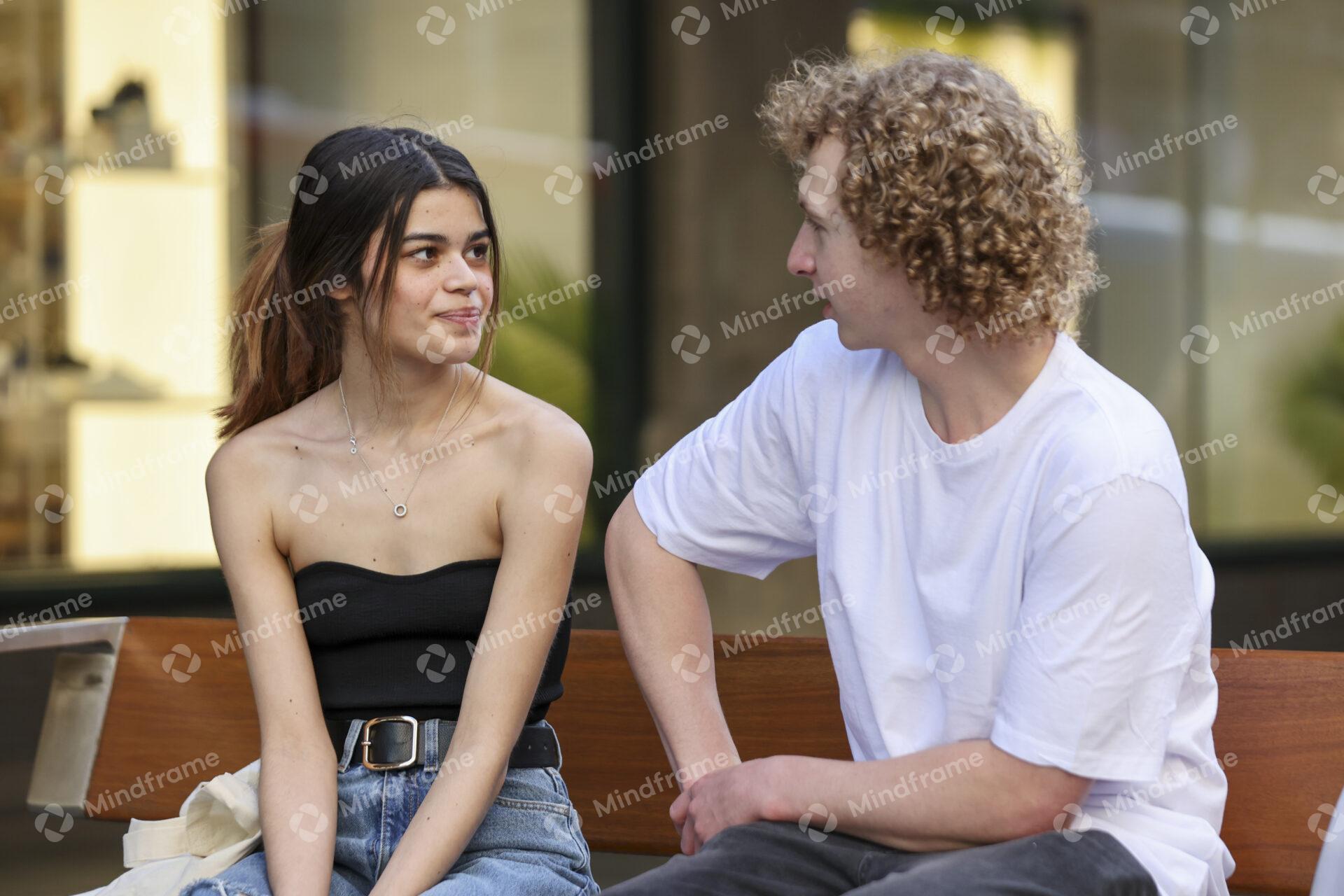 Two people talking while seated on a bench in an urban landscape