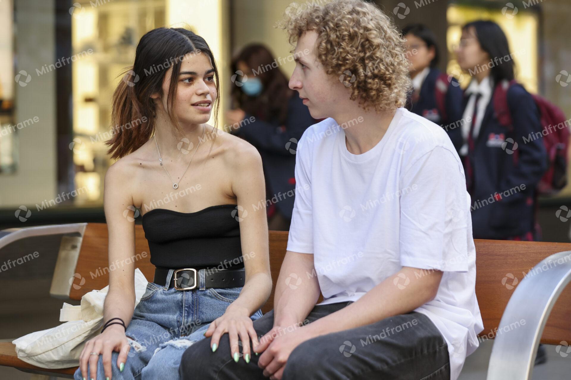 Two people talking while seated on a bench in an urban landscape