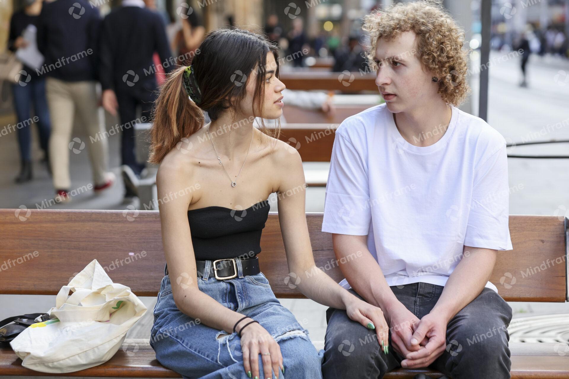 Two people talking while seated on a bench in an urban landscape