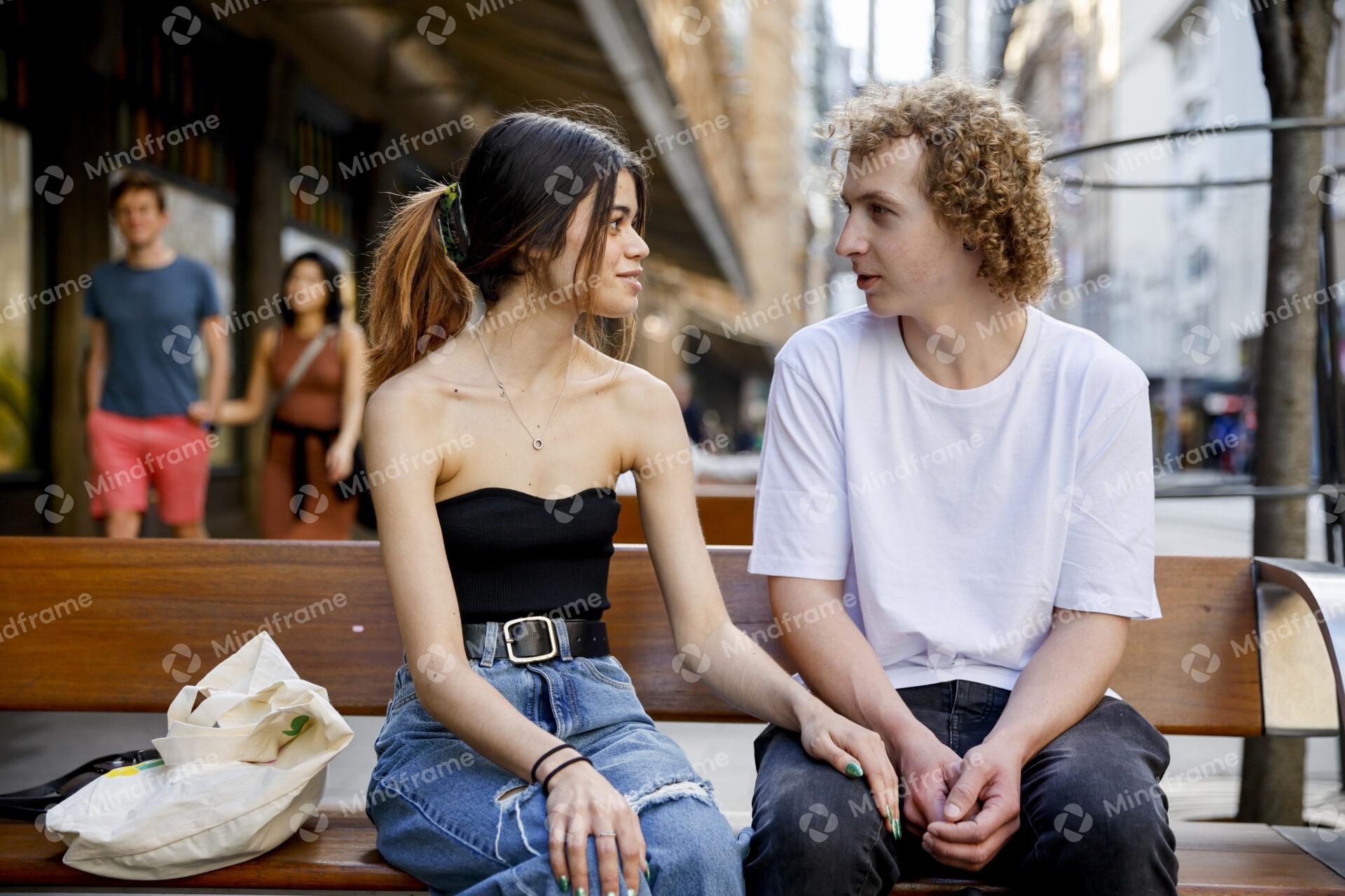 Two people talking while seated on a bench in an urban landscape