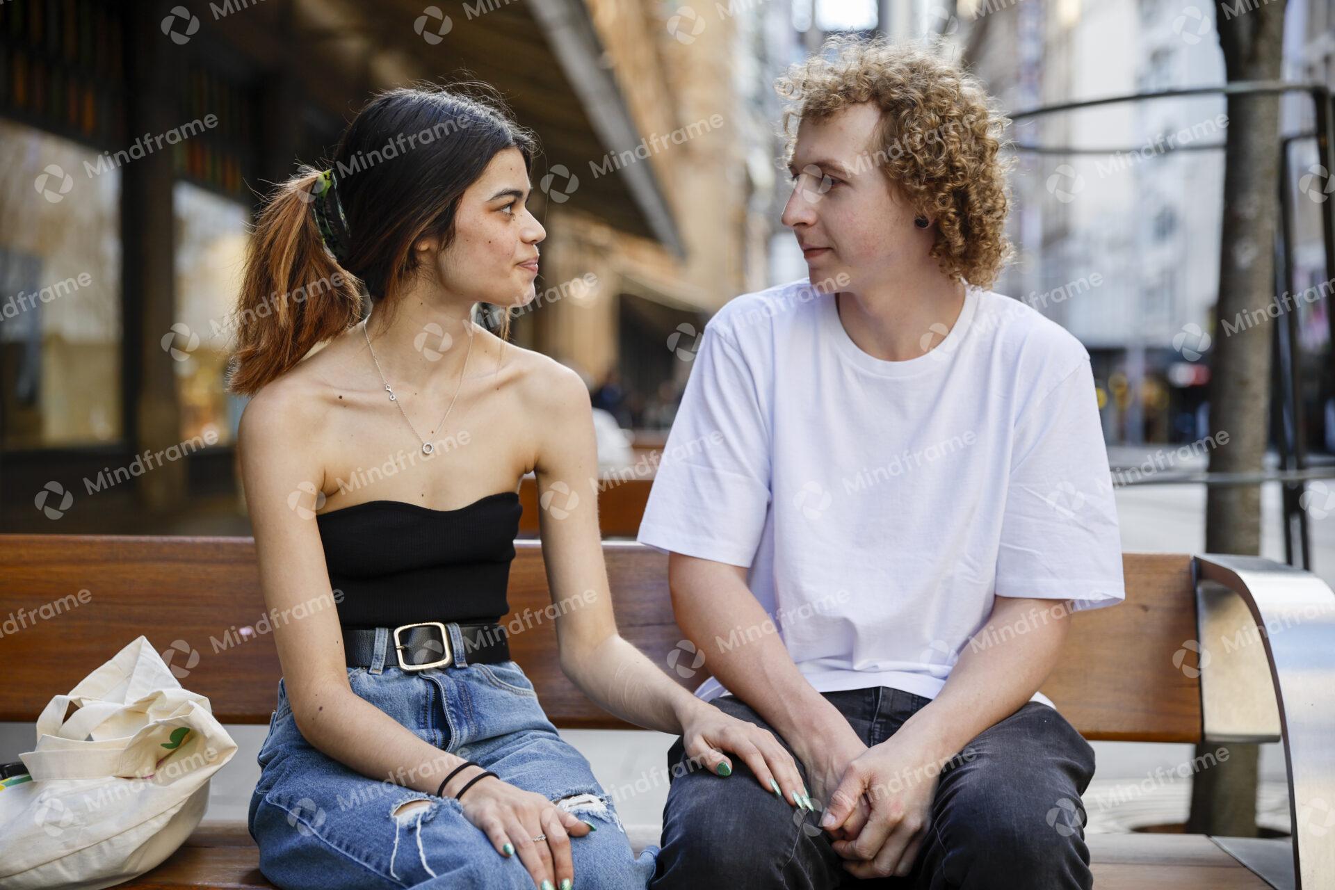 Two people talking while seated on a bench in an urban landscape