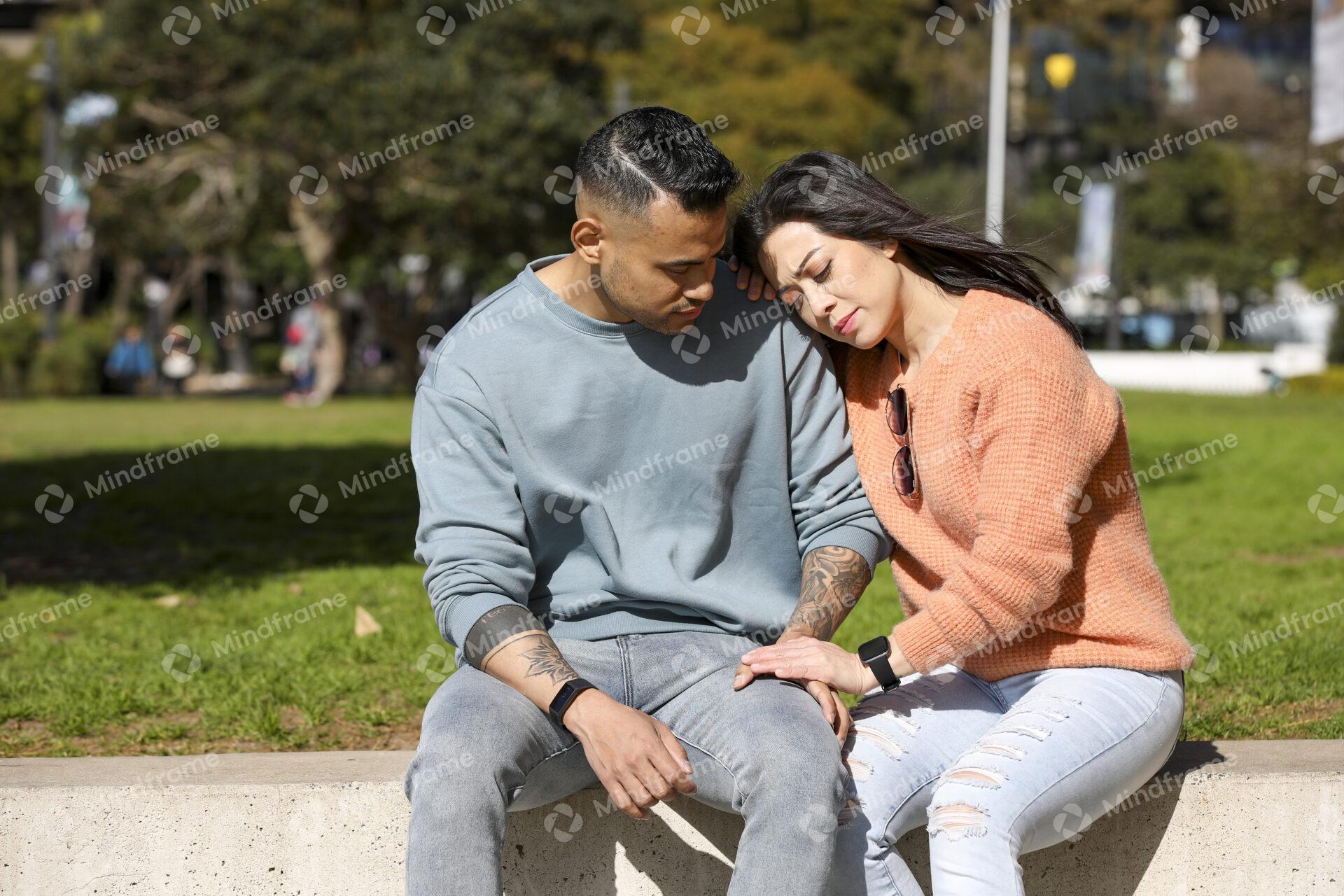 Two people sitting on bench outdoors supporting each other