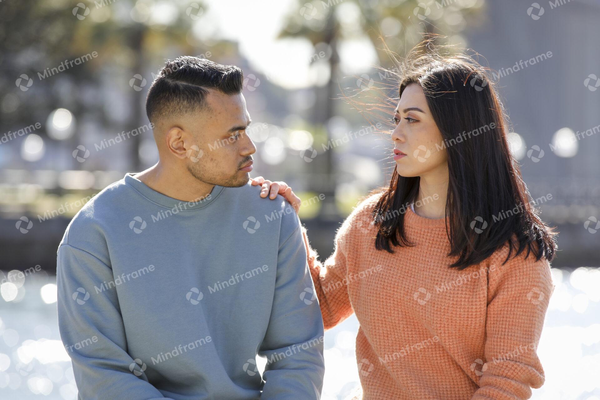 Two people sitting on a bench in front of the harbour and looking at each other