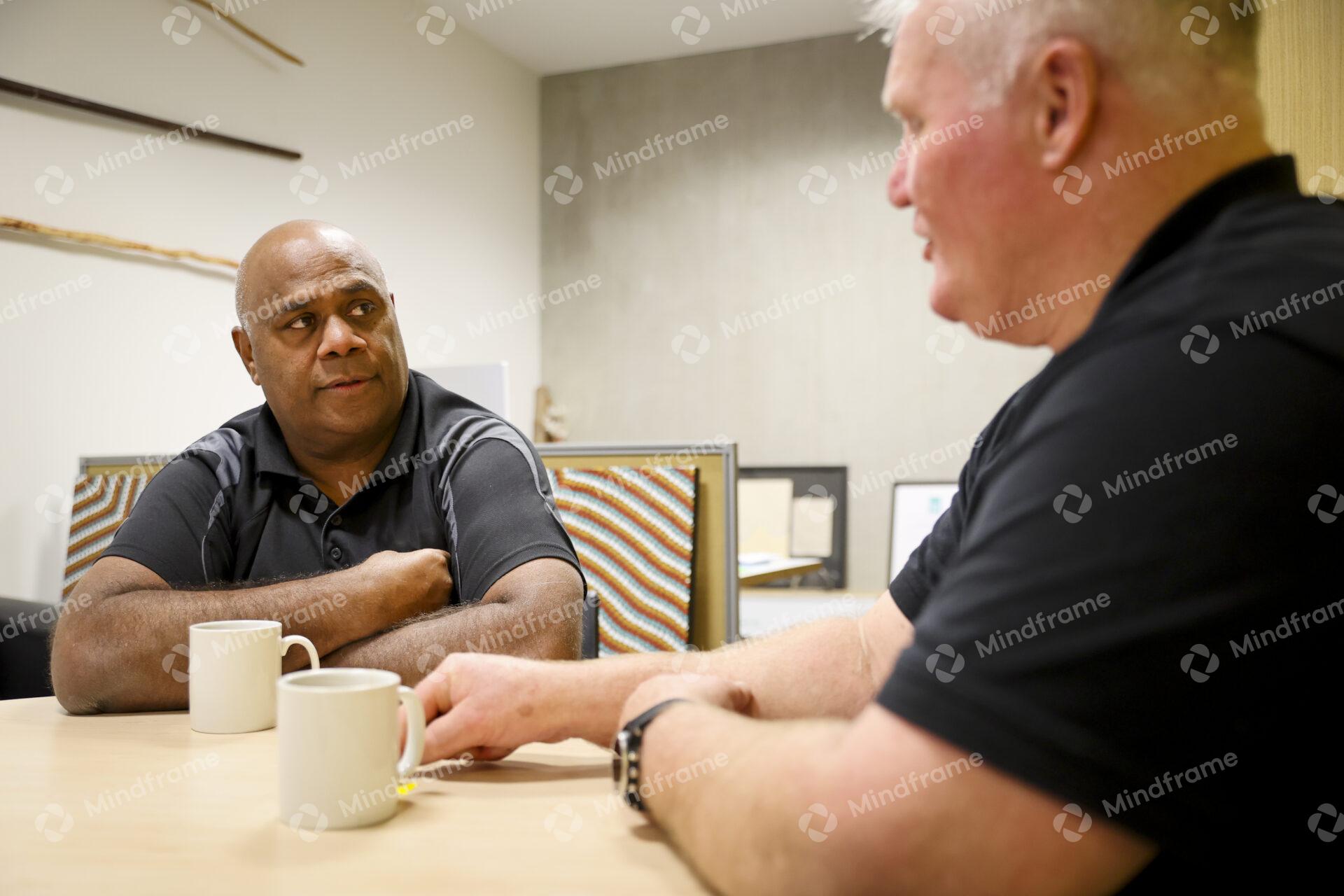Two men sitting at a table indoors having a conversation