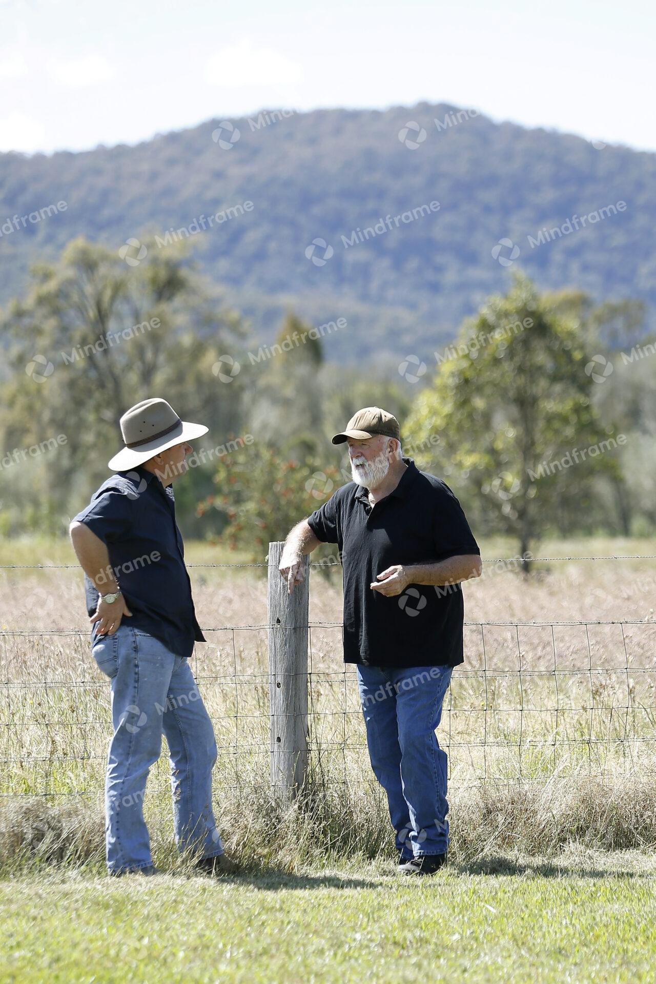 Two people standing by a paddock fence at a farm