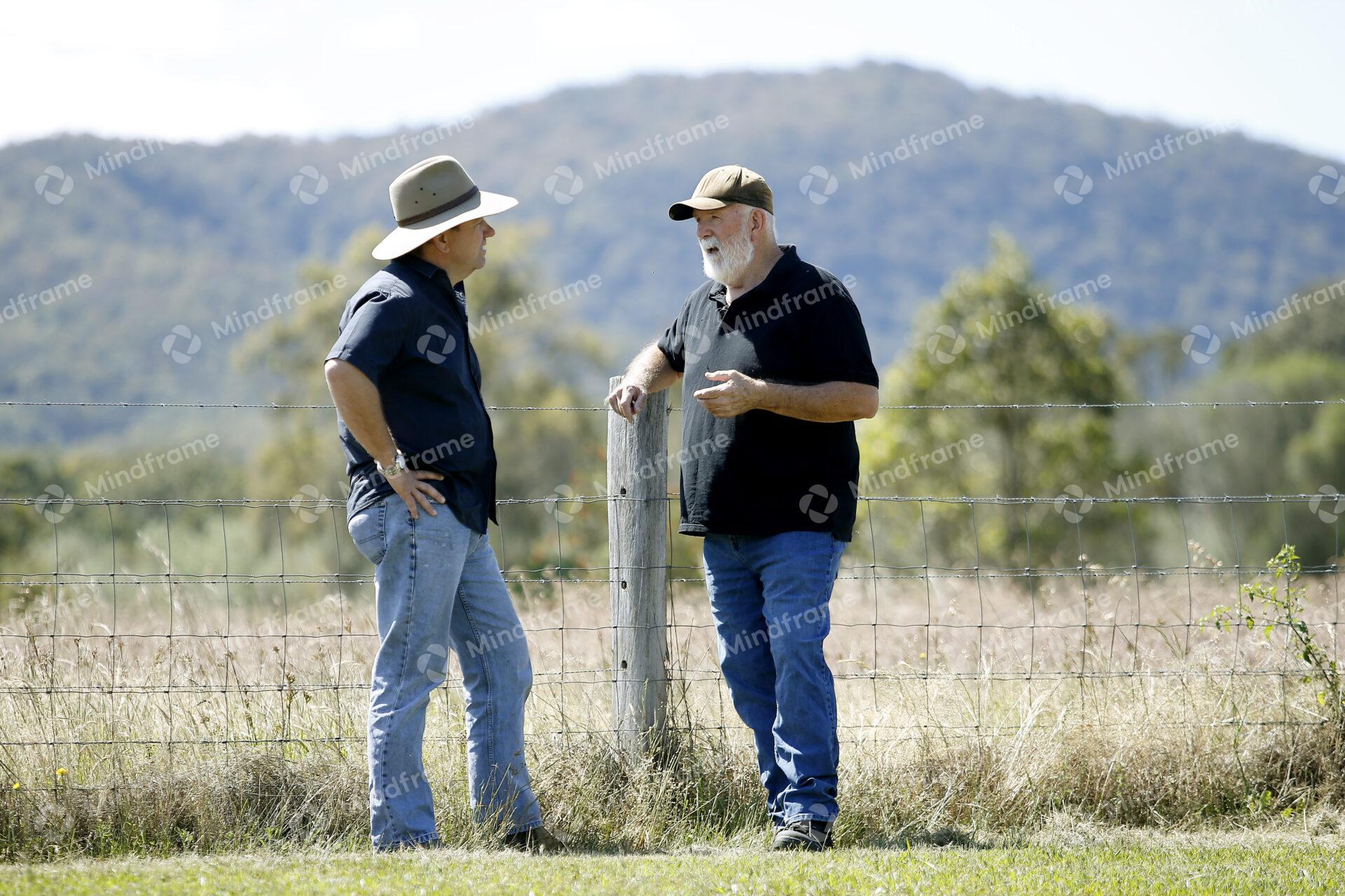 Two people standing by a paddock fence at a farm