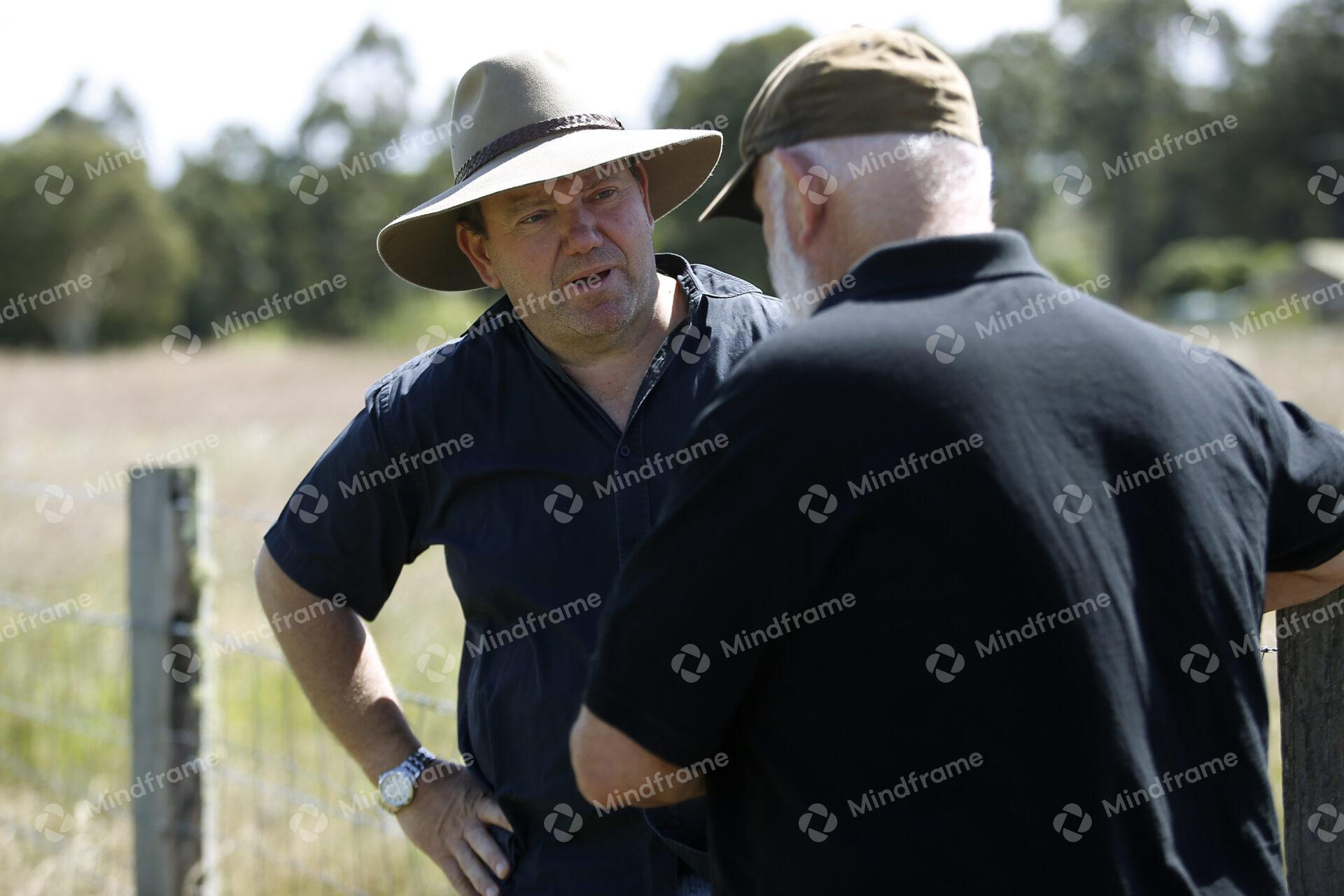 Two people standing by a paddock fence at a farm