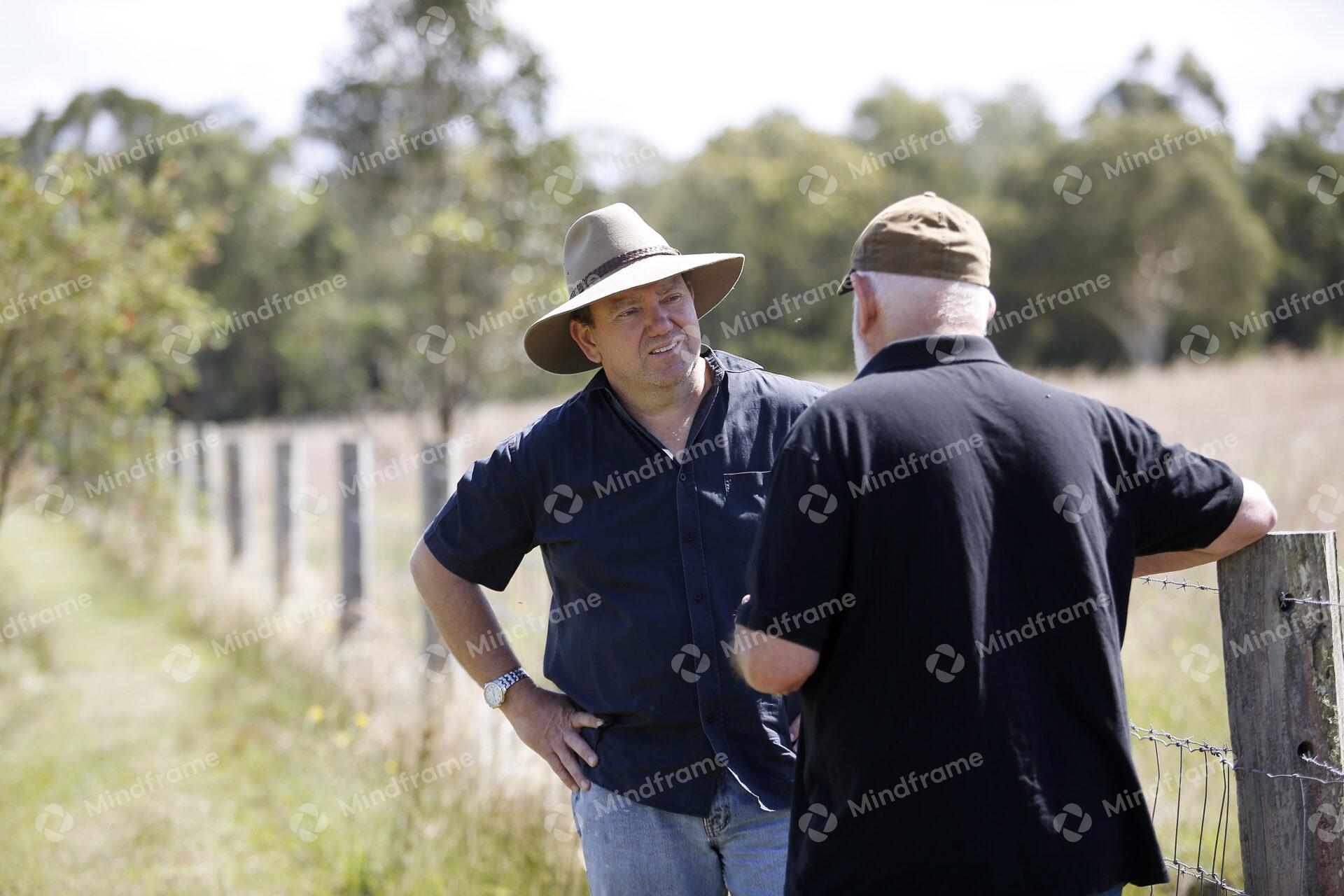 Two people standing by a paddock fence at a farm