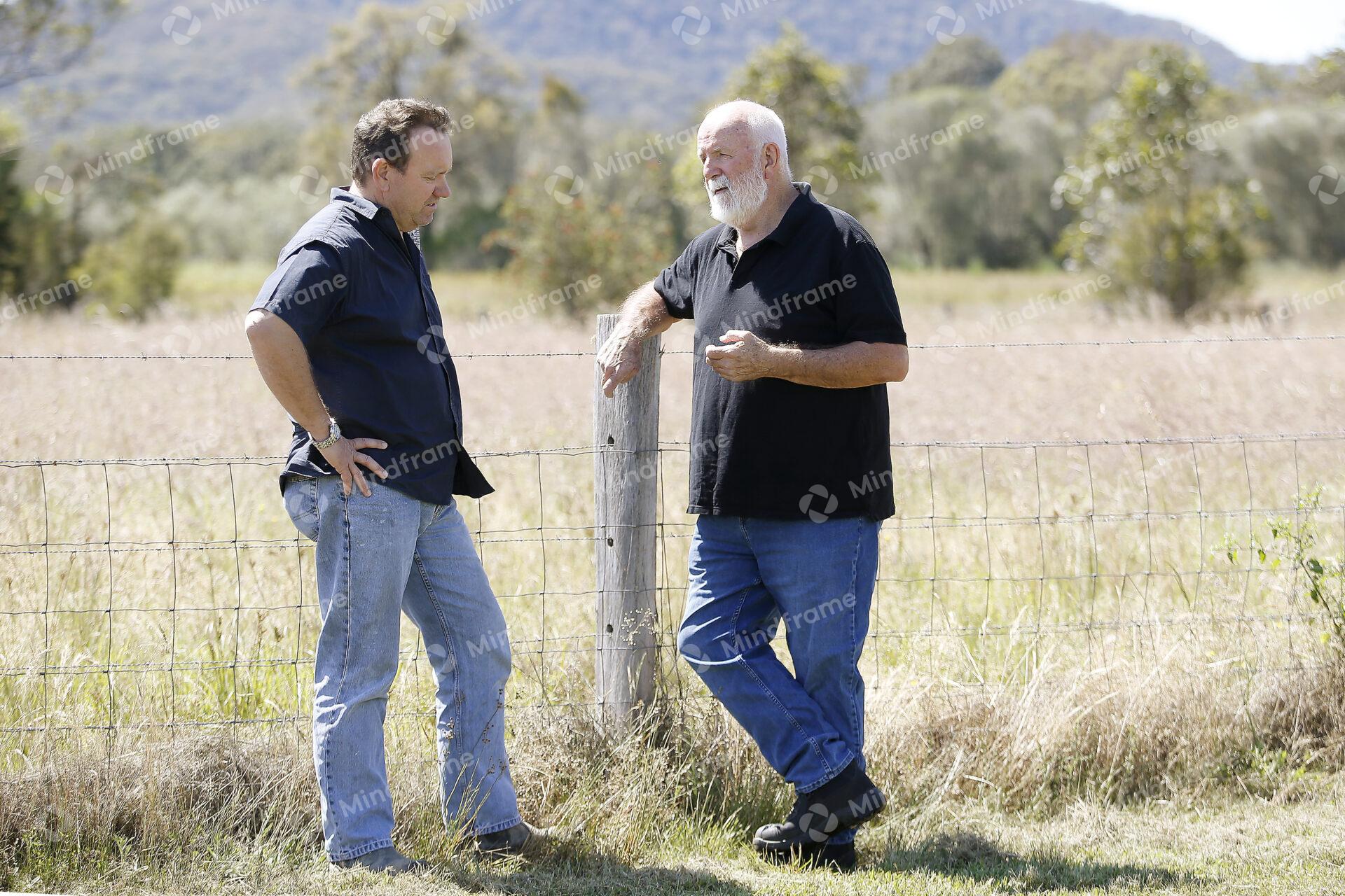 Two people standing by a paddock fence at a farm
