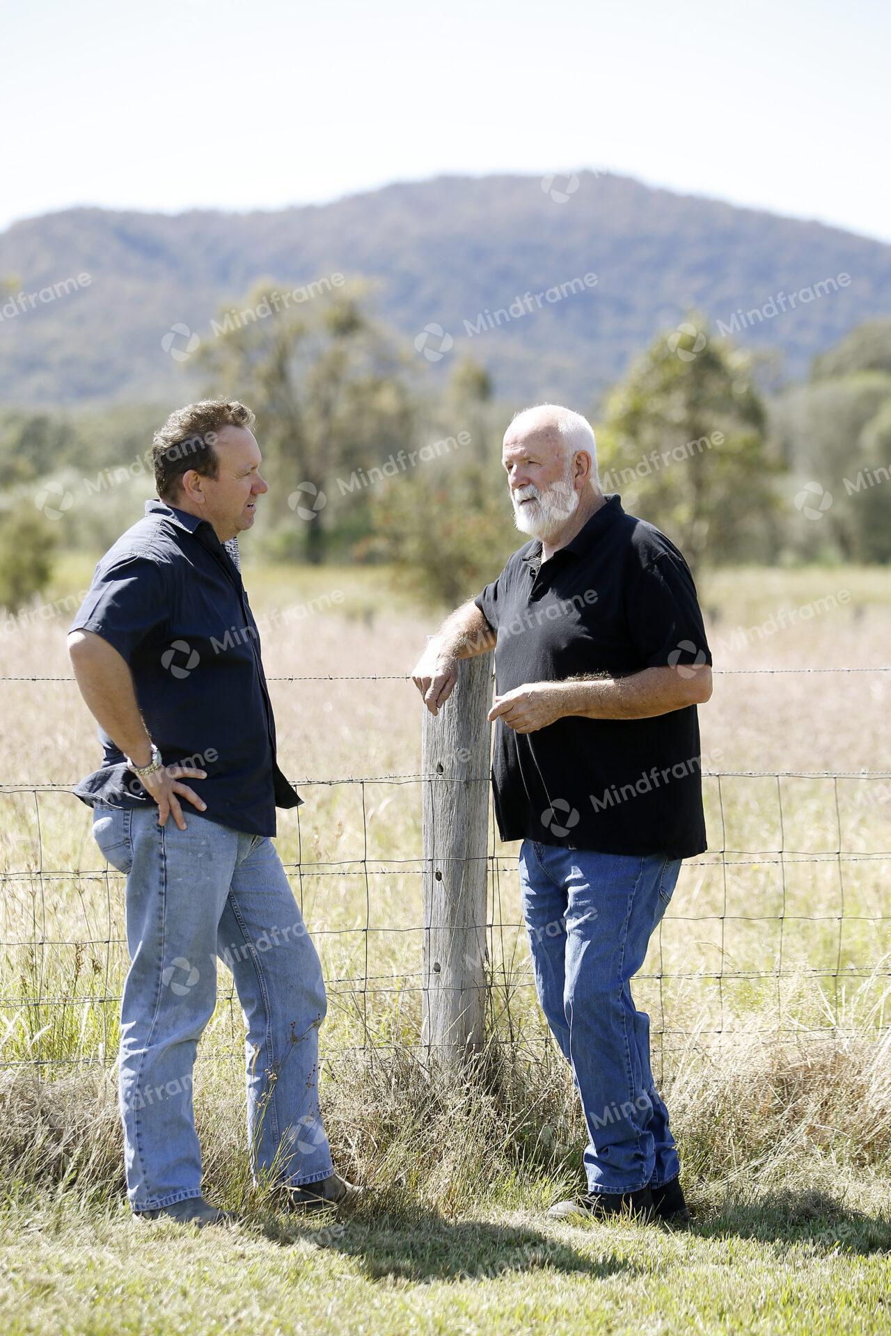 Two people standing by a paddock fence at a farm