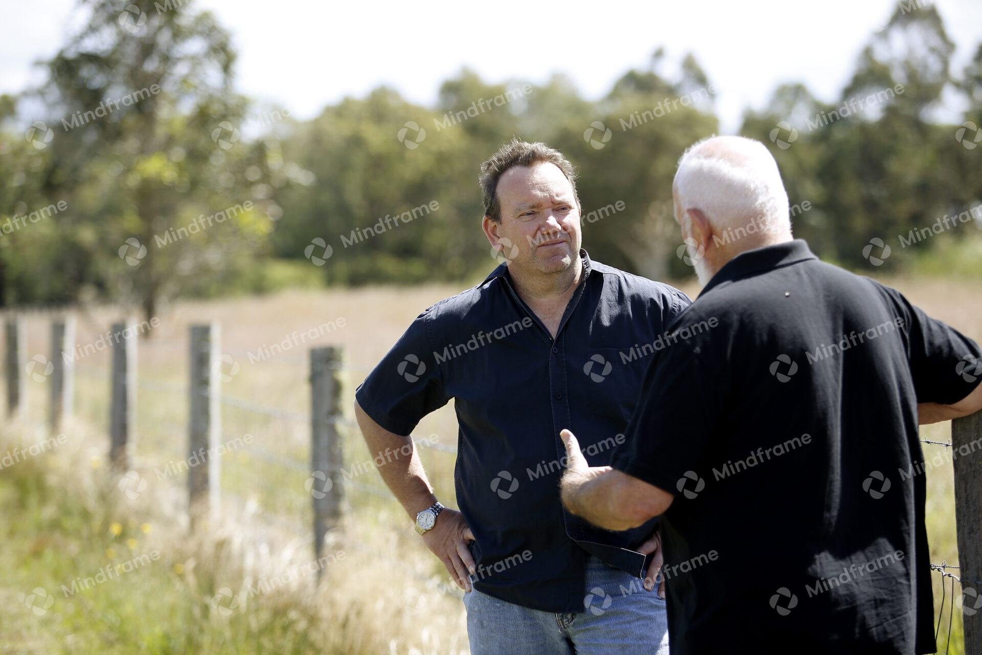 Two people standing by a paddock fence at a farm