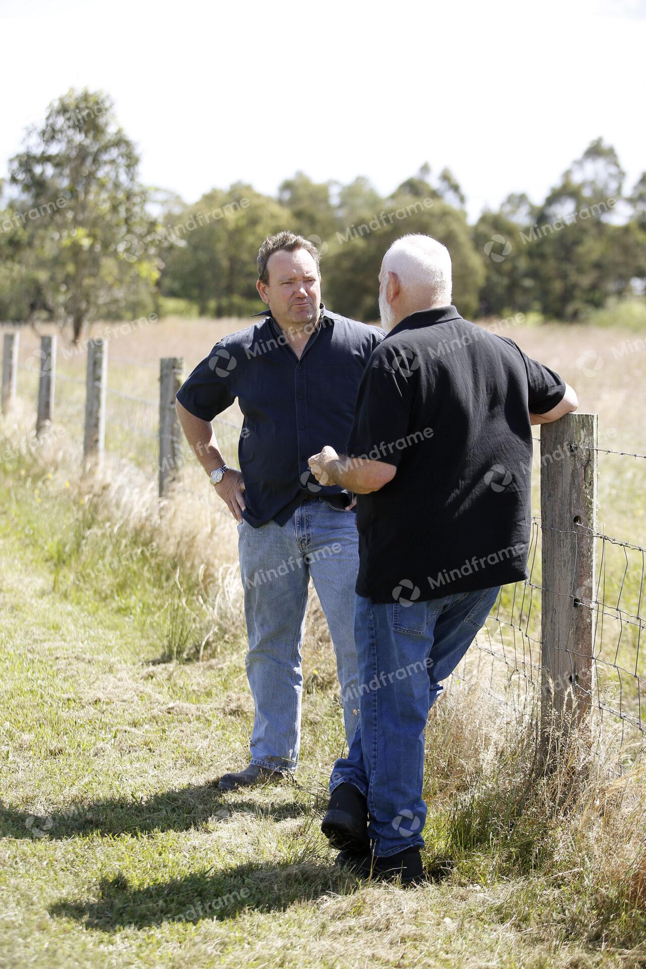 Two people standing by a paddock fence at a farm