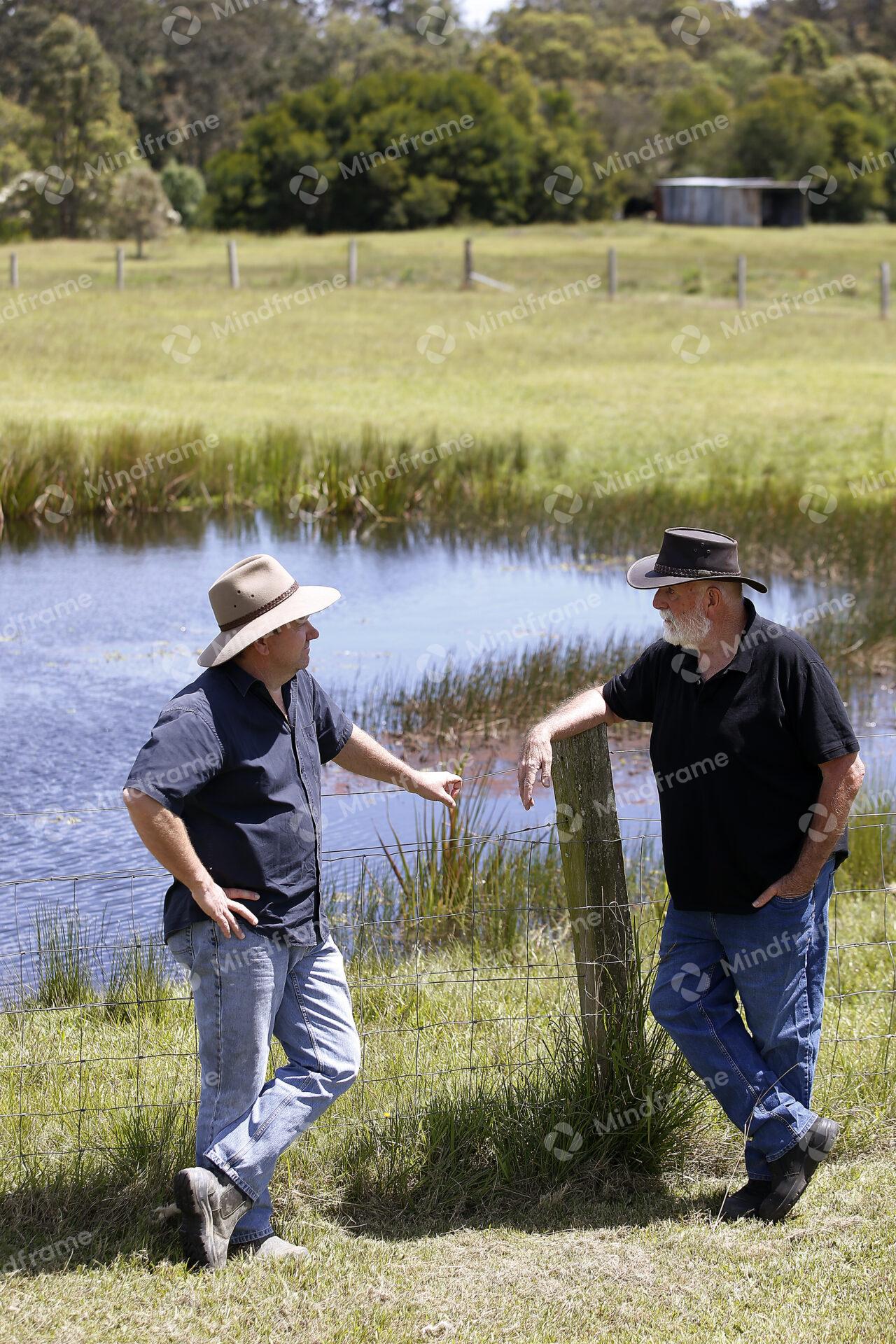 Two people leaning on a fence by a dam at a farm