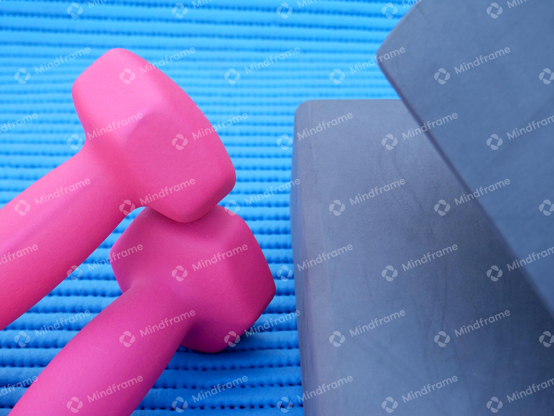 Pink weights and yoga blocks on a exercise mat close up